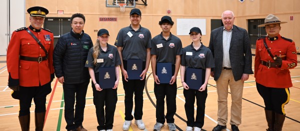 Four Youth Academy students smile beside two RCMP members, the Mayor of Burnaby and a City Councillor inside a school gymnasium
