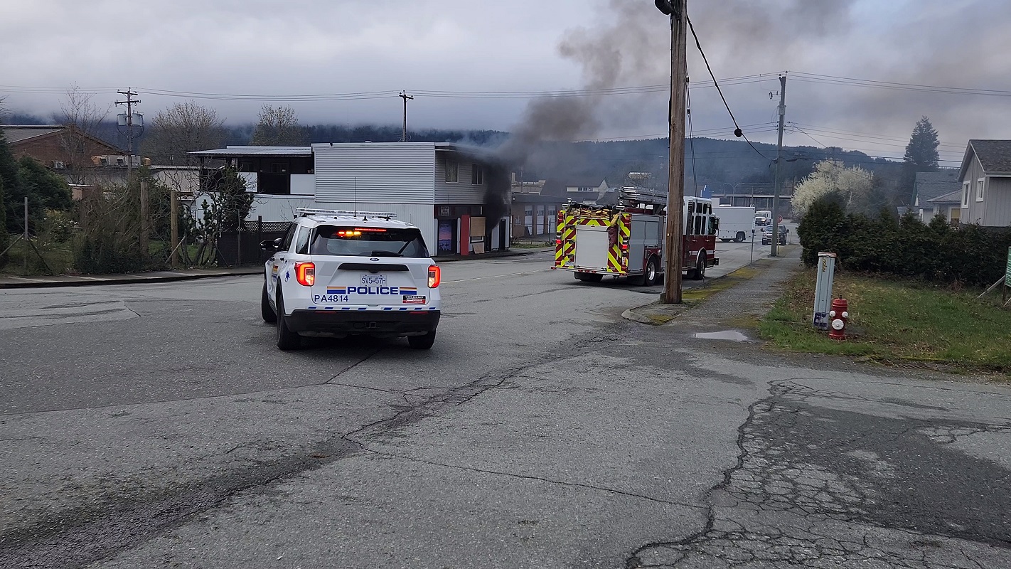 An RCMP vehicle and a fire truck infront of a house with smoke coming out of the front