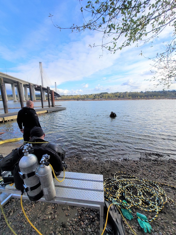 One RCMP Underwater Recovery Team officer is in the water while another diver sits along the shore