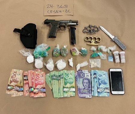 An image of package drugs, cash, a cellphone, and weapons including a pistol, knife, and brass knuckles, are displayed on a table as evidence.  