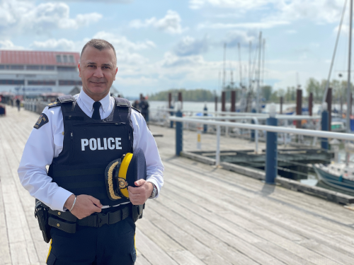 Chief Superintendent Dave Chauhan, Officer in Charge of Richmond RCMP standing holding his hat in his hands and smiling against a sunny outdoor backdrop