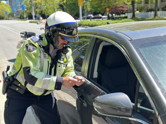 Richmond RCMP officer wearing a motorcycle helmet checking a driver&rsquo;s license beside a vehicle