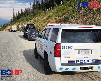 A police vehicle with a tow truck towing 2 vehicles on a highway