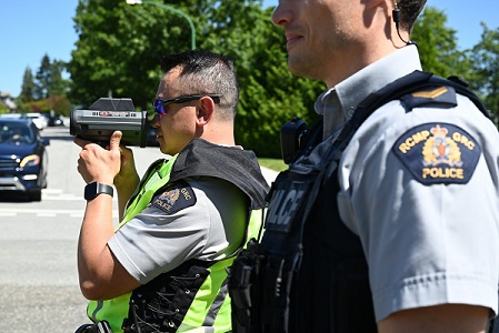 Des agents de la GRC de Burnaby en uniforme en bordure de route par une journ&eacute;e ensoleill&eacute;e. L&rsquo;un d&rsquo;eux utilise un d&eacute;tecteur de vitesse laser. 