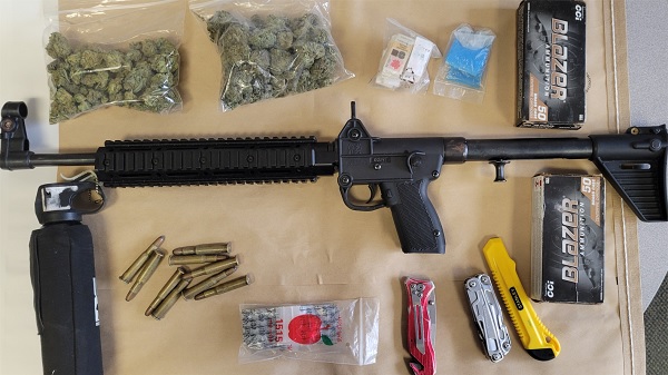 Firearm, cannabis, knives, ammunition and drug paraphernalia displayed on table.