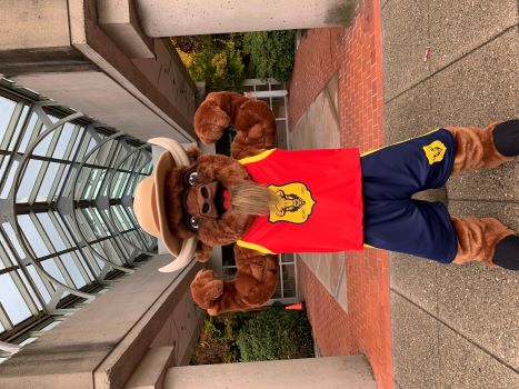 Une mascotte de bison en uniforme de basketball portant un maillot de basketball rouge de la GRC, des shorts de basketball bleus et un chapeau Stetson brun devant l&rsquo;immeuble du D&eacute;tachement de la GRC de Surrey.