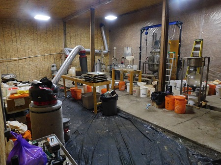 A large room with drug making materials including silver piping, a hoist and numerous plastic buckets.