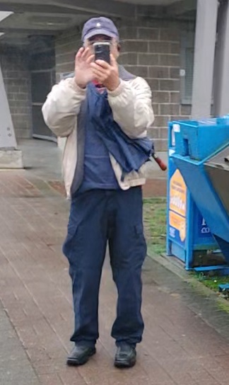 Person of interest wearing a blue baseball hat, blue shirt, beige jacket, blue pants and black shoes