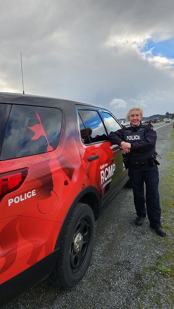 Photo of Cst. Sam Haldane in uniform standing next to her recruiting vehicle showing the rear of the vehicle. 
