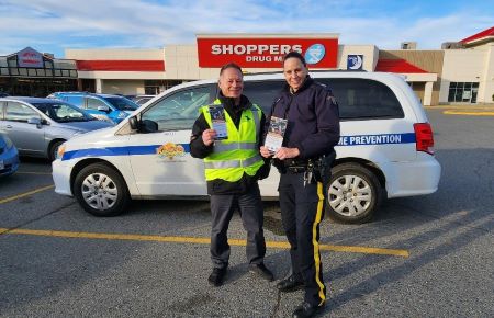 Two members of the Kamloops RCMP Crime Prevention Team hold information cards with tips to hand out, in a retail parking lot.