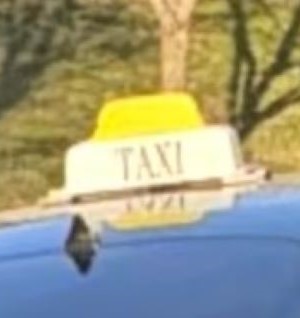 A closeup image of a yellow and white taxi sign on top of a dark vehicle&rsquo;s roof