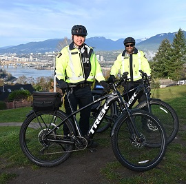 Deux policiers portant une veste r&eacute;fl&eacute;chissante se tiennent avec des v&eacute;los &eacute;lectriques devant eux et des montagnes en arri&egrave;re-plan. 