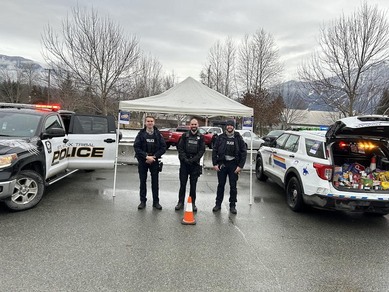A photo of two RCMP police officers and one Stl'atl'imx Tribal Police Officer standing between two police vehicles with mountains in the background