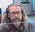 A Caucasian man with long brown hair and a full trimmed beard, wearing glasses and a black jacket.