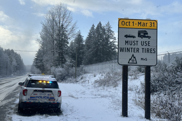 A BC Highway Patrol vehicle parked by a sign that says vehicles must use winter tires