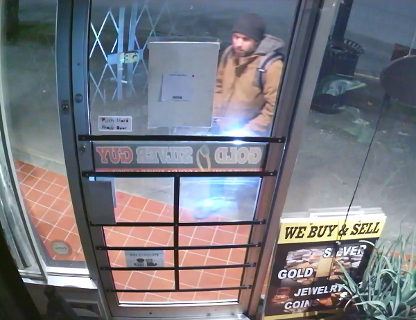 suspect standing in front of the store door, wearing a black toque, brown jacket and brown boots.