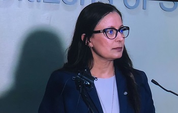 Le caporal Dhesi porte un blazer et des lunettes s&rsquo;adressant aux m&eacute;dias.