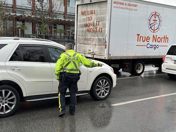 A BC Highway Patrol standing beside a vehicle and waving a distracted driver to the side of the road
