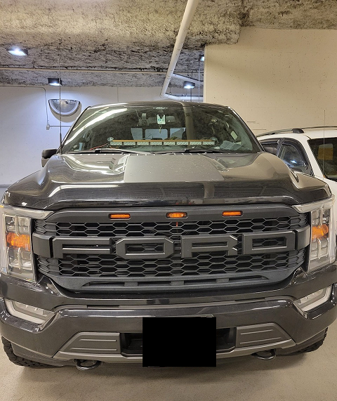 Picture of a black Ford F150 truck with a light bar placed on the lower centre of the windshield, which resembles lighting used on police vehicles.