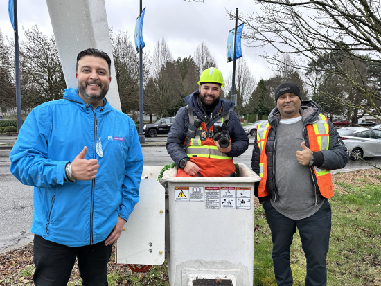 Deux hommes, le pouce levé, se tiennent de part et d'autre d'un homme installé dans une nacelle élévatrice et muni d’un appareil photo
