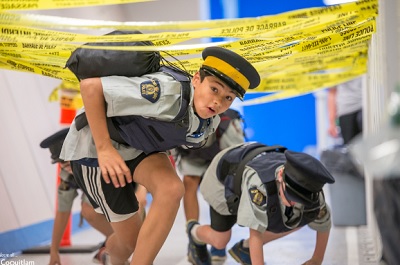 Youth wearing RCMP short sleeve shirt and RCMP forage cap crawling through obstacle course.