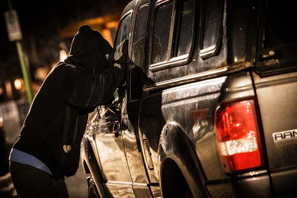Photo of man in dark clothes looking through driver side window of a truck