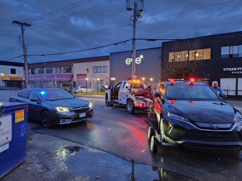 Black sedan loaded on to tow truck with lights flashing, beside an unmarked police vehicle