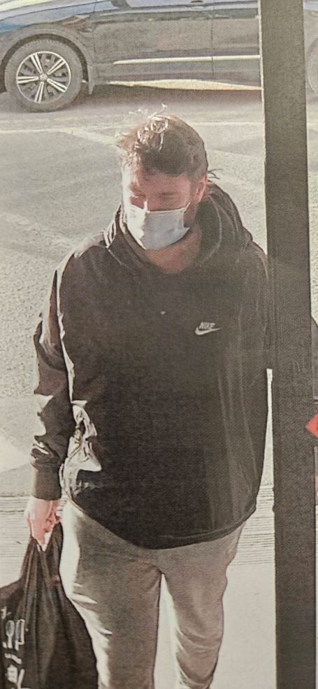 Le suspect franchit une porte, v&ecirc;tu d&rsquo;une veste Nike fonc&eacute;e et d&rsquo;un pantalon beige, tout en tenant un sac noir avec des &eacute;critures blanches.