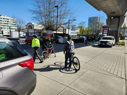 un agent de la GRC de Richmond vêtu d’une veste à haute visibilité, avec deux cyclistes sur le trottoir.