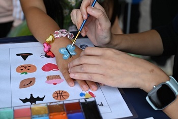 A youth getting their hand painted with a blue butterfly. 