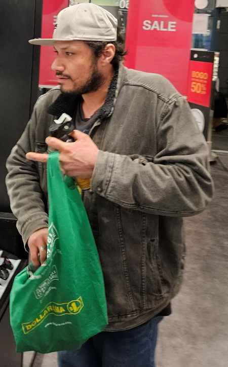 Photo of male suspect wearing a beige baseball hat, dark denim jacket, black shirt, blue jeans and was carrying a green reusable shopping bag and holding a cannister in his hand