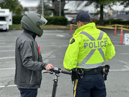 Richmond RCMP officer standing beside e-scooter rider