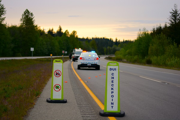A BC Highway Patrol vehicle sits behind a &lsquo;DUI checkpoint&rsquo; sign as a vehicle is towed away for impaired driving