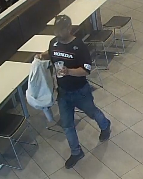 suspect in black t-shirt, dark baseball cap and blue jeans walking