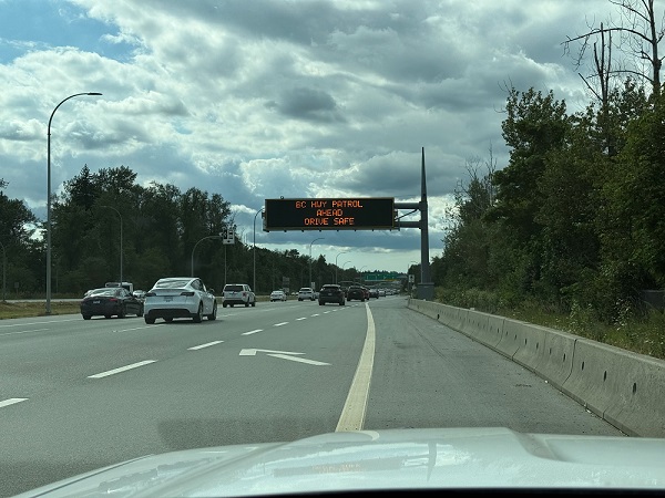 A police photo showing traffic flow under a sign displaying <q>BC Hwy Patrol Ahead. Drive Safe.</q> Moments after this photo, a prohibited driver was stopped for speeding while using his cell phone 