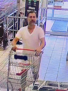 Le troisi&egrave;me suspect pousse un chariot dans le magasin. Il porte un t shirt blanc &agrave; encolure en V et un short de couleur p&acirc;le. Il a les cheveux fonc&eacute;s courts et porte une barbe grisonnante ou naissante. 