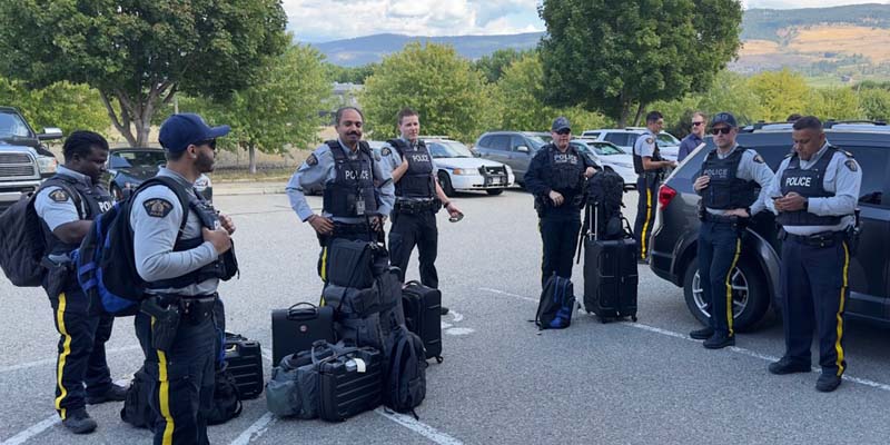 Several officers in uniform are welcomed to Kelowna by another officer who is also in uniform. 