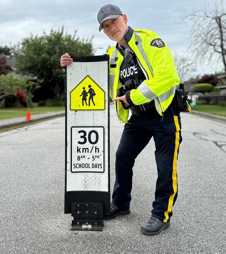 Photo d'un policier avec un panneau sur lequel il est &eacute;crit : &laquo; 30 km/h de 8 h &agrave; 17 h les jours d&rsquo;&eacute;cole &raquo;. 