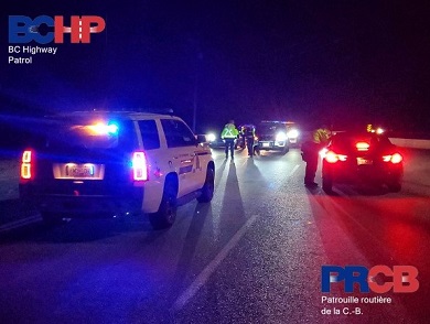Night time photo of a police road check with uniformed officer checking a vehicle