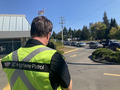 Officer with &lsquo;BC Highway Patrol&rsquo; emblazoned on the back of his vest watches traffic through a spotting scope