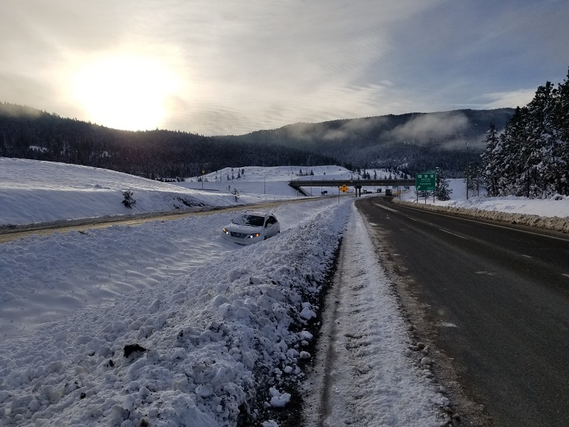 A white sedan in the center median of highway 5, stuck in the snow.