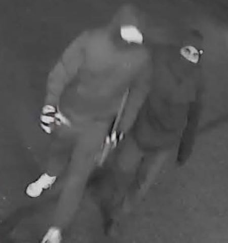 Deux suspects portant des vestes &agrave; capuchon et des masques sont film&eacute;s en train de marcher dans une vid&eacute;o de surveillance en noir et blanc. 