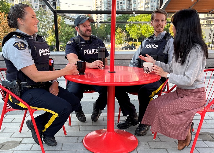 Police officers sitting outside around a table while drinking coffee and talking to the public
