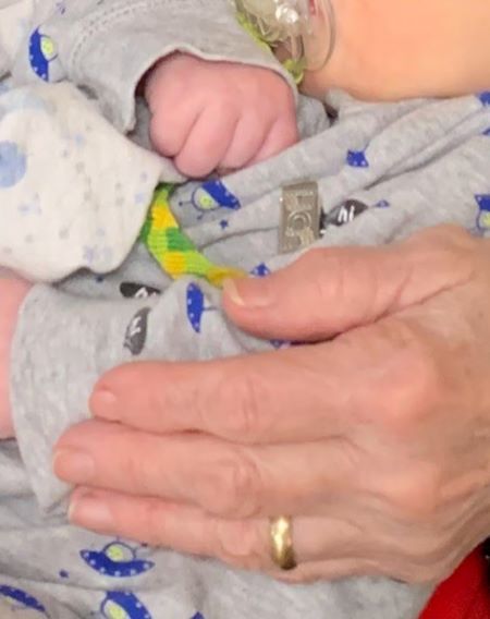 Une alliance en or &agrave; l&rsquo;annulaire d&rsquo;une femme qui tient un b&eacute;b&eacute; envelopp&eacute; d&rsquo;une couverture.