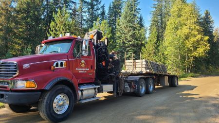 A side profile of a large red semi truck and trailer. A decal for &lsquo;Kamloops Hiab Services&rsquo; is on the driver&rsquo;s side door. 