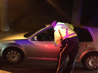 Uniformed police officer looks into the window of a vehicle stopped at the roadside