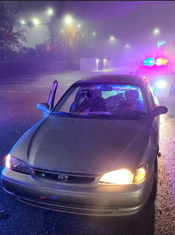 Photo of police car with its lights on behind a car with one headlight out