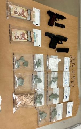 Guns, packaged drugs, and cash are displayed on a table.