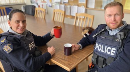 Deux policiers sont assis &agrave; une table pour la pause-caf&eacute;. L&rsquo;un tient une tasse rouge, l&rsquo;autre une noire. 