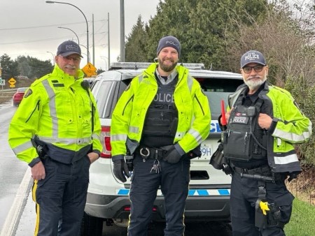 Photo of three Richmond RCMP officers standing in front of a police vehicle on the side of the road]